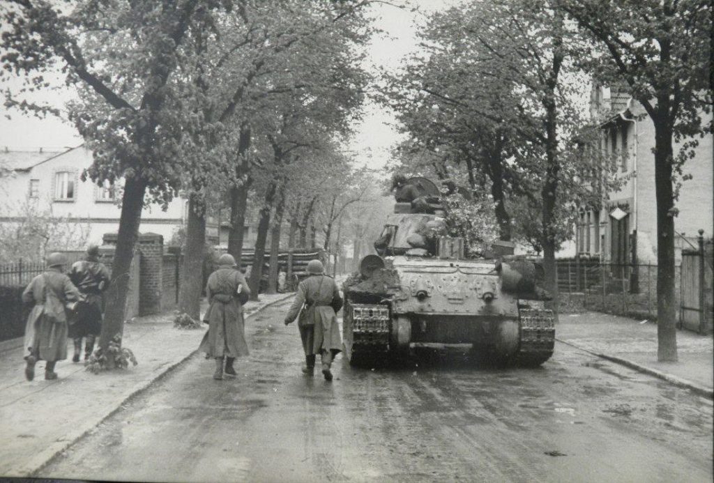 Red Army troops advance into Berlin's suburbs alongside a Soviet tank